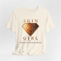 Cream unisex t-shirt featuring the Skin Girl™ shield logo and the phrase Protect Your Barrier in bronze and gold tones.