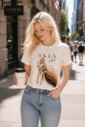 Woman wearing Skin Girl Fitz I Radiant esthetician graphic t-shirt walking through downtown city street with coffee in hand.